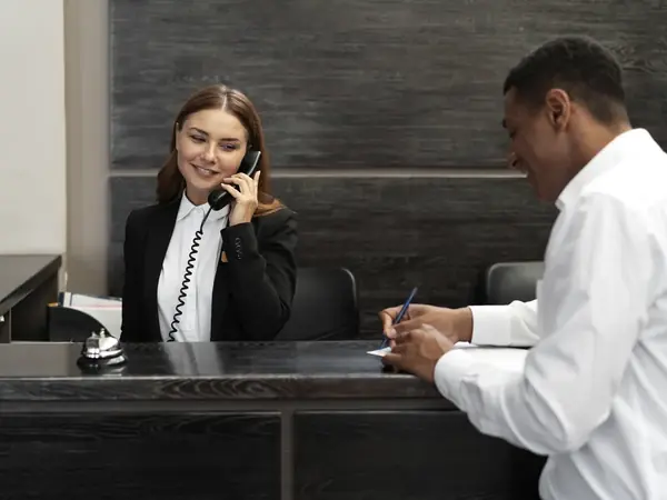 Recepcionista atendiendo una llamada mientras un visitante firma en el mesón