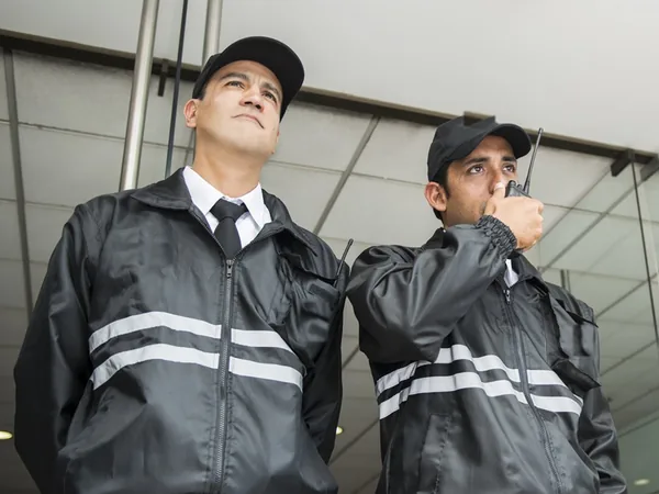 Dos guardias de seguridad vigilando el acceso de un edificio, uno de ellos hablando por radio